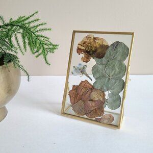 Standing brass and glass picture frame with dry flowers arrangement.